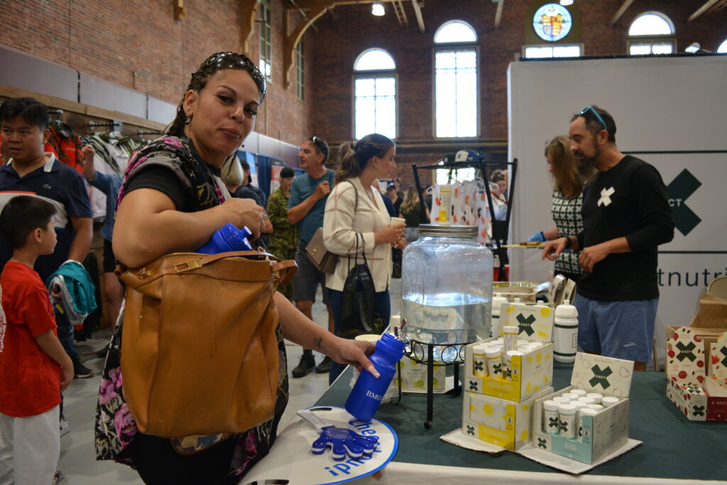 A woman fills her water bottle at the xact nutrition table. | Une femme remplit sa bouteille d'eau à la table xact nutrition.