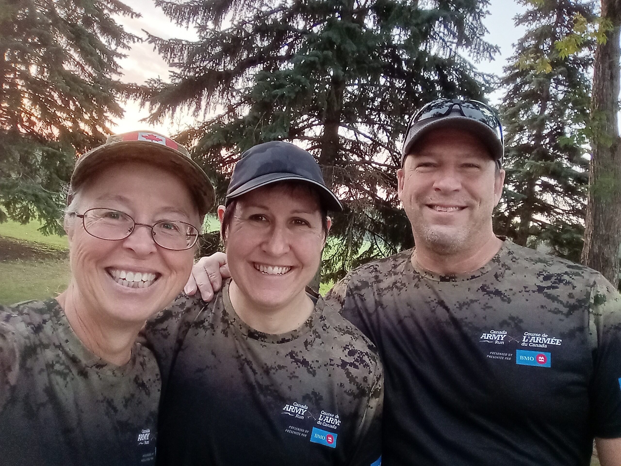 Three smiling people wear Canada Army Run shirts. | Trois personnes souriantes portent des chandails de la Course de l'Armée du Canada.