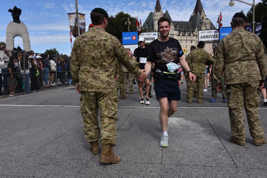 A runner is congratulated by a member of the Canadian Army after crossing the finish line. | Un coureur est félicité par un membre de l'Armée canadienne après avoir franchi la ligne d'arrivée.