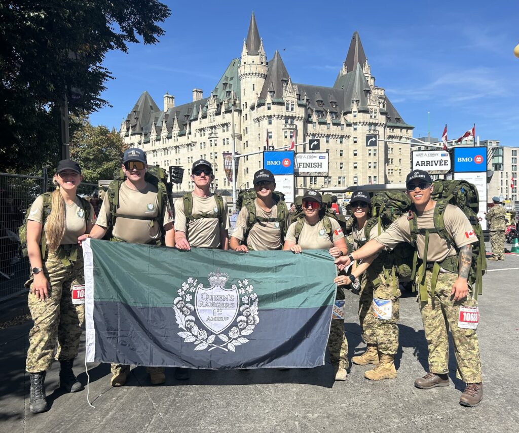 Men and women in uniform pose with their regimental flag after crossing the Canada Army Run finish line. | Des hommes et des femmes en uniforme posent avec leur drapeau de régiment après avoir franchi la ligne d’arrivée de la Course de l’Armée du Canada.
