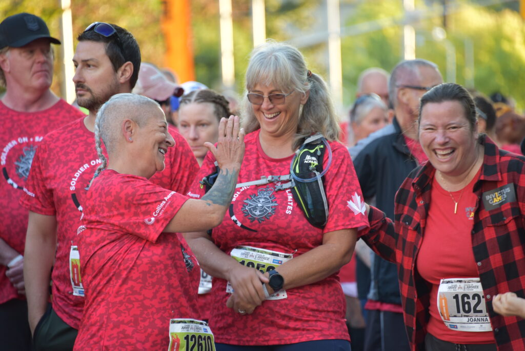 Three women laugh on the start line, as one goes in for a high five. | Trois femmes rient sur la ligne de départ, tandis que l’une d’elles tend la main pour un « high five ».